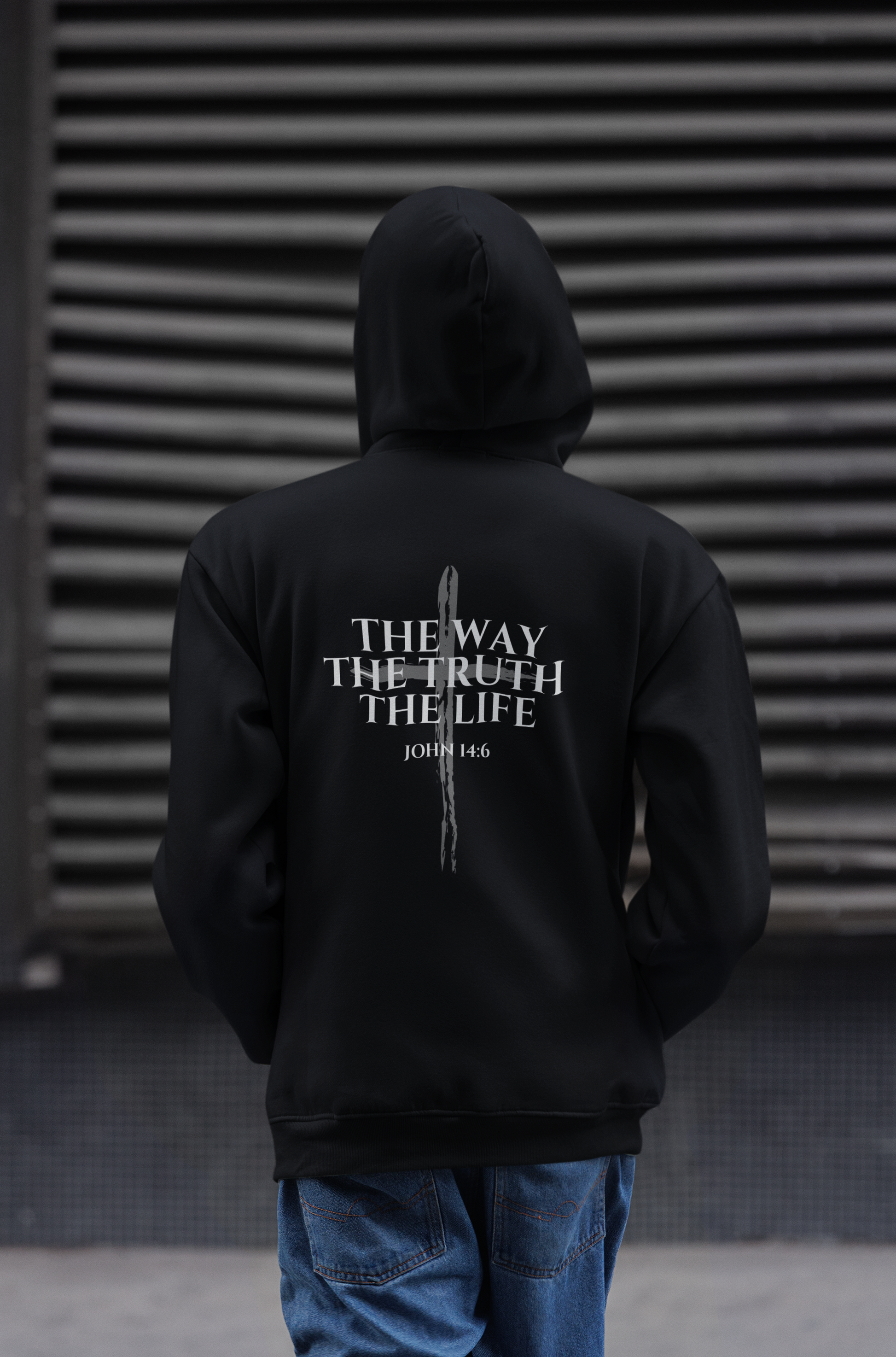 Man wearing a Black Christian hoodie featuring "John 14:6 I am the way, the truth, and the life" printed design, faith-based streetwear for men and women, bold minimalist scripture hoodie from Let There Be Light Apparel