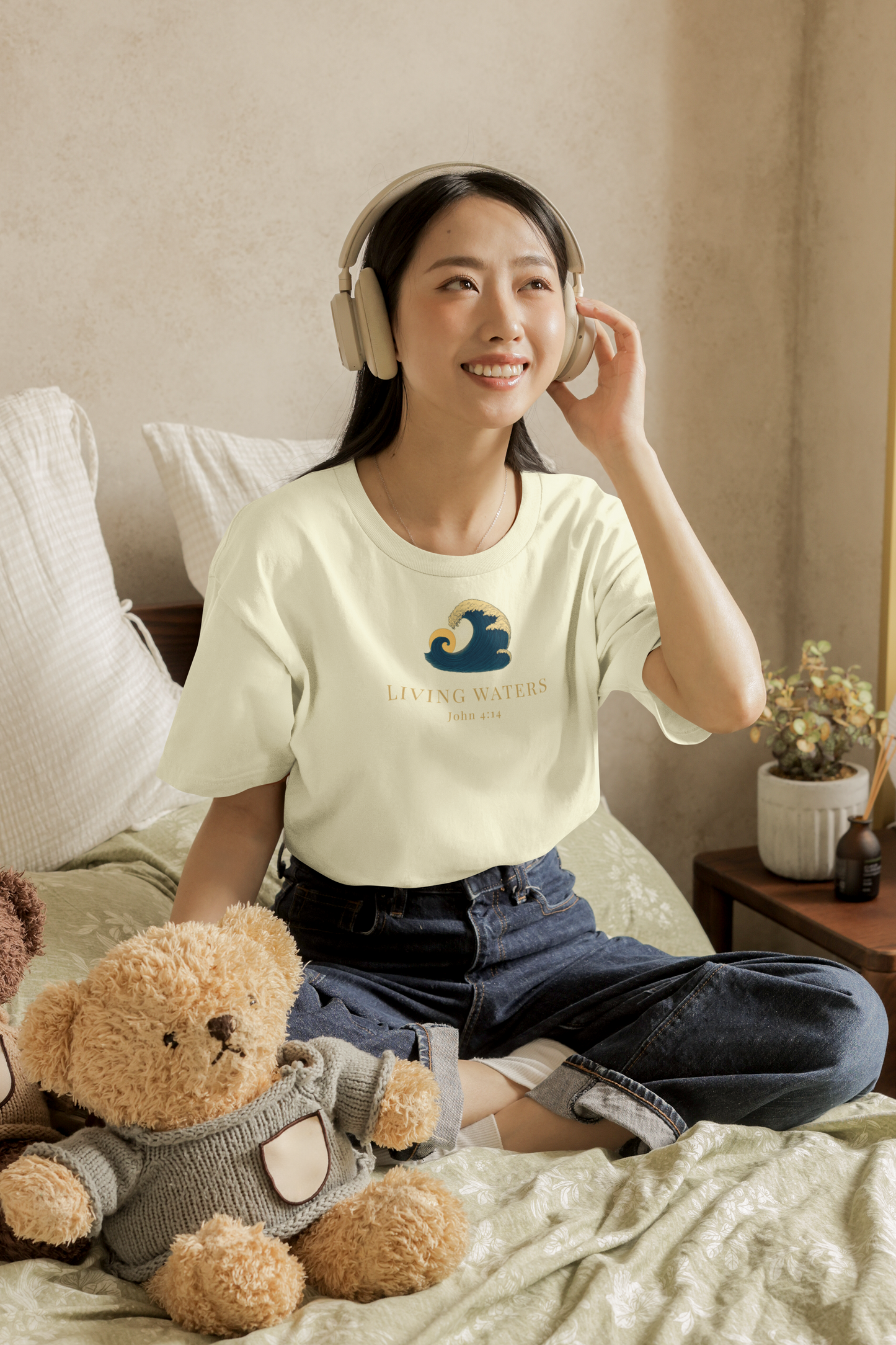 Woman sitting on a bed wearing headphones and a t-shirt with a logo, surrounded by teddy bears.