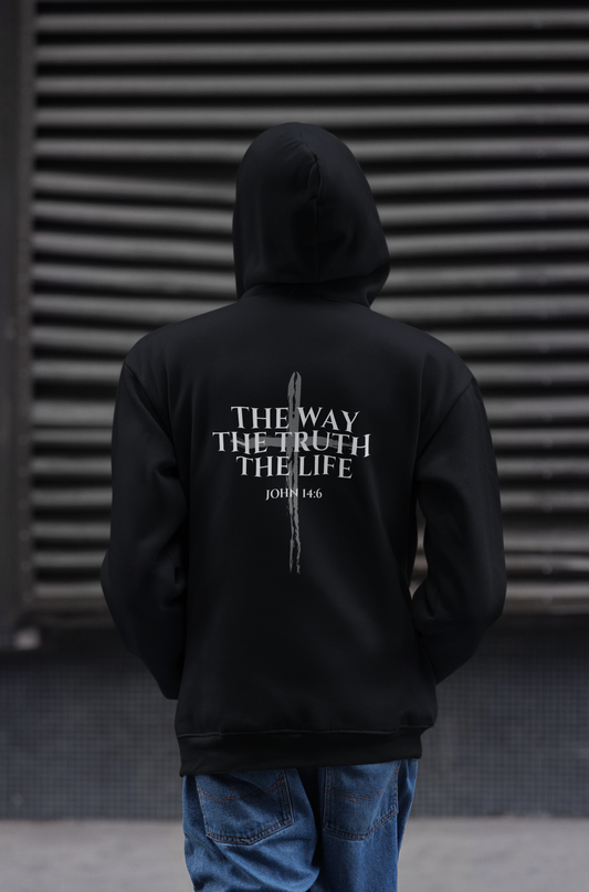 Man wearing a black Catholic hoodie featuring the John 14:6 Bible verse, "The Way, The Truth, The Life," with a cross design on the back. Modern faith-based apparel inspired by Jesus Christ for Catholics, and anyone who wants to wear their faith with confidence.